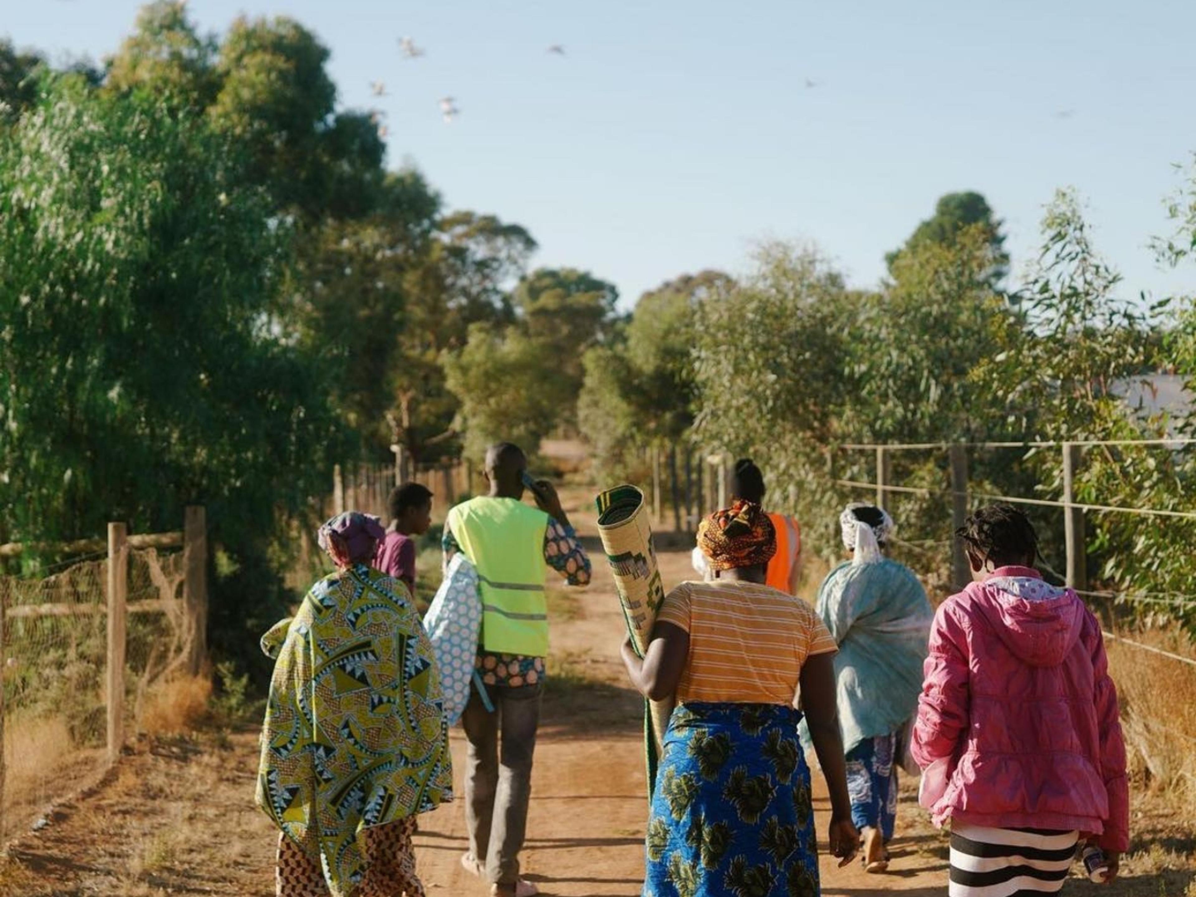 A group of people walking down a dirt track on a sunny day.