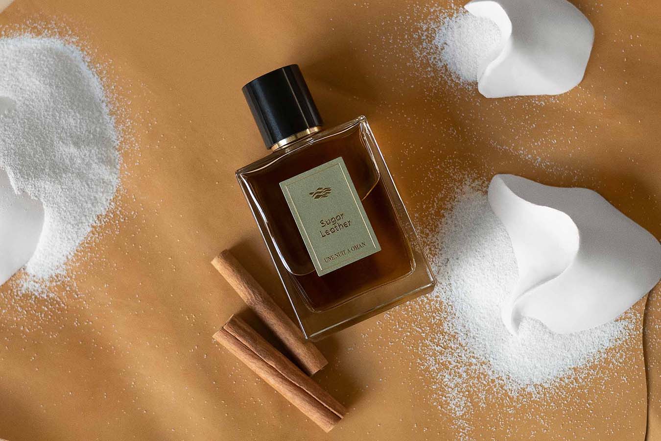 En flaska av parfymen "Sugar Leather" från Une Nuit Nomade omgiven av socker och kanelstänger.
