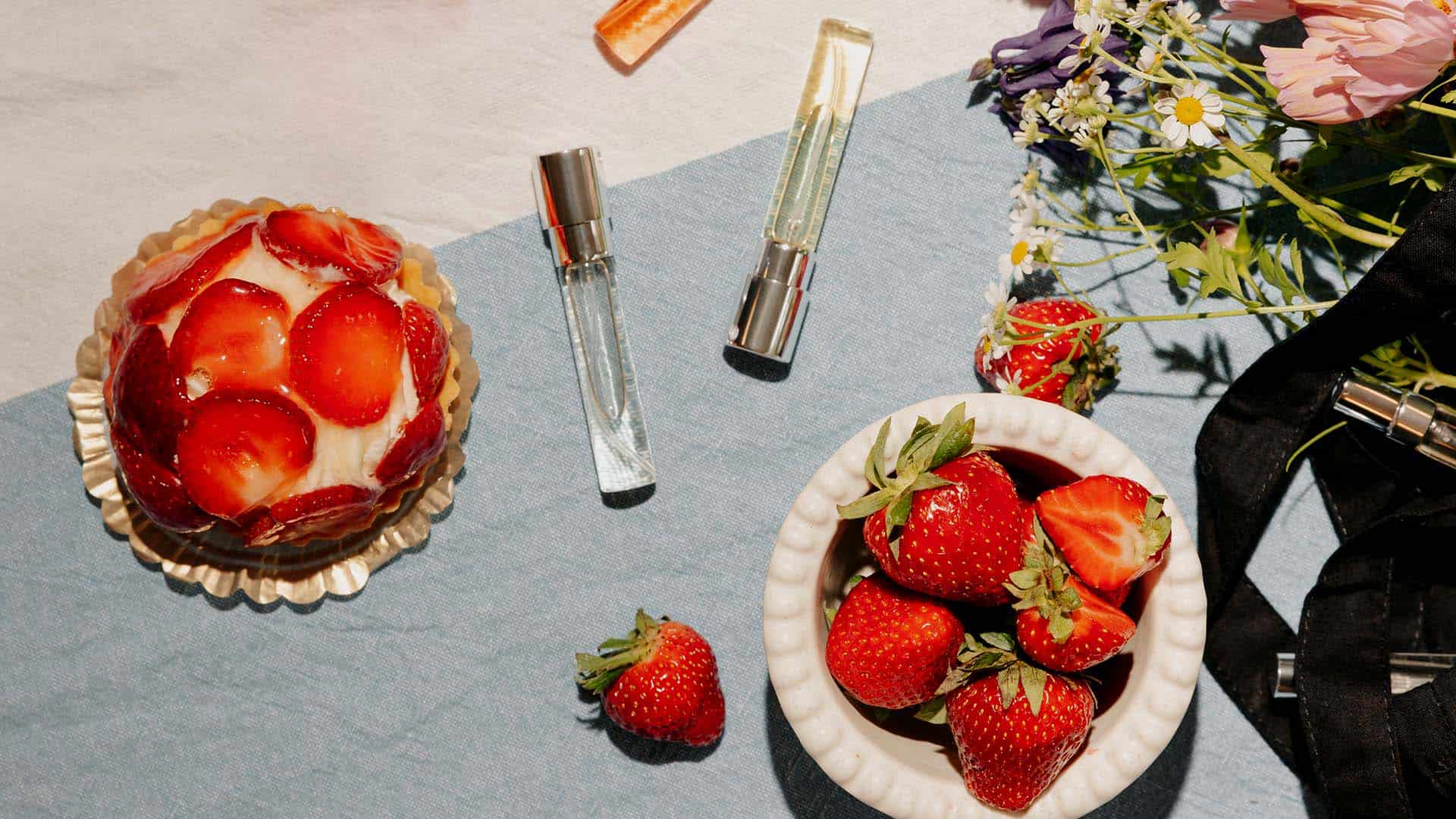 Sniph 8 ml perfume bottles on a blue and white fabric with strawberry cakes, flowers, and fresh strawberries