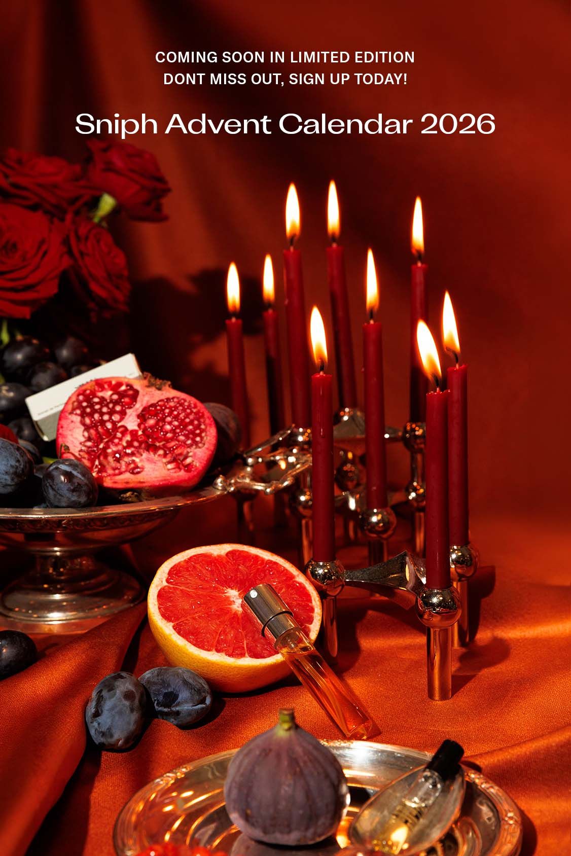 Ett stilleben med tända ljus, frukt i silverfat och parfymflaskor på en orange bakgrund.
