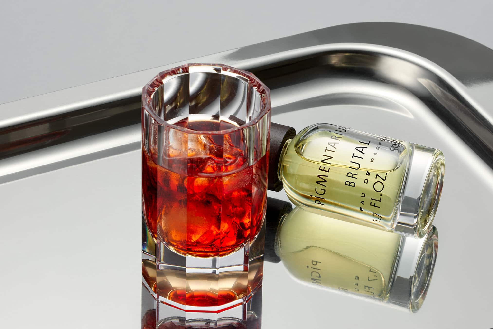 Doften Brutal från Pigmentarium på en silverbricka bredvid en Negroni-drink.