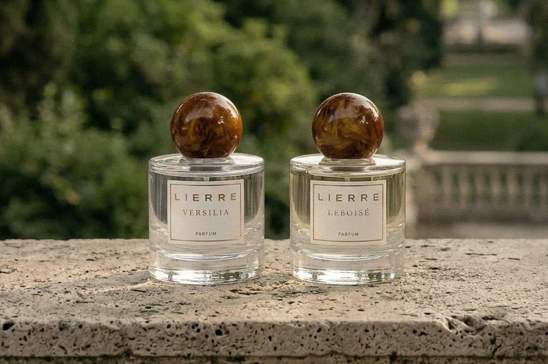 The two Lierre perfumes sitting on a stone wall with a lush landscape as a backdrop.