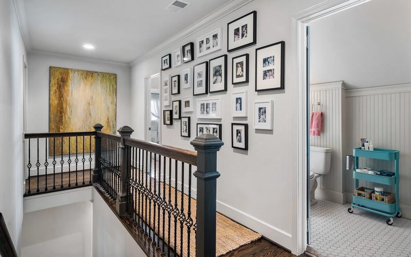 Black-framed family photos arranged on a gallery wall above the staircase landing of a Birmingham home, capturing generations of memories in a single hallway.