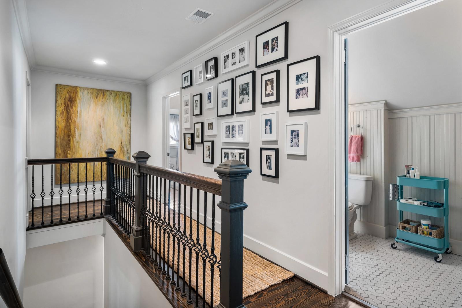 Black-framed family photos arranged on a gallery wall above the staircase landing of a Birmingham home, capturing generations of memories in a single hallway.