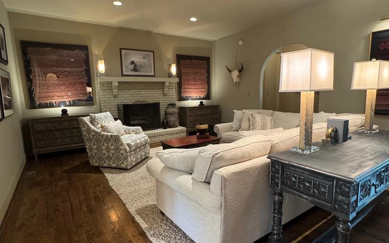 A spacious family room with rich hardwood floors, a brick fireplace flanked by Southwestern textile art, generous sectional seating, and warm lamp light — the kind of well-loved gathering room found in many established Birmingham homes.