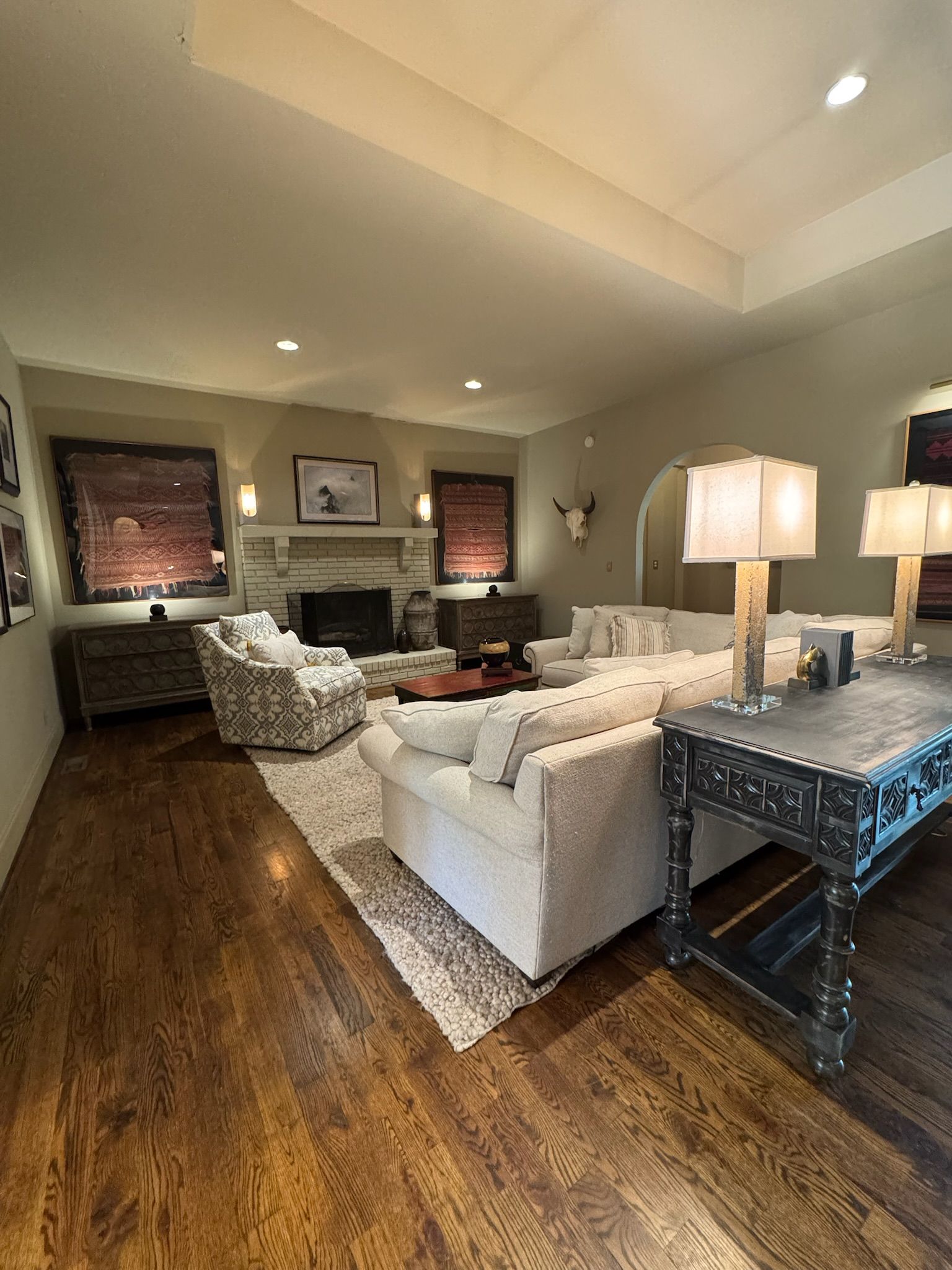 A spacious family room with rich hardwood floors, a brick fireplace flanked by Southwestern textile art, generous sectional seating, and warm lamp light — the kind of well-loved gathering room found in many established Birmingham homes.