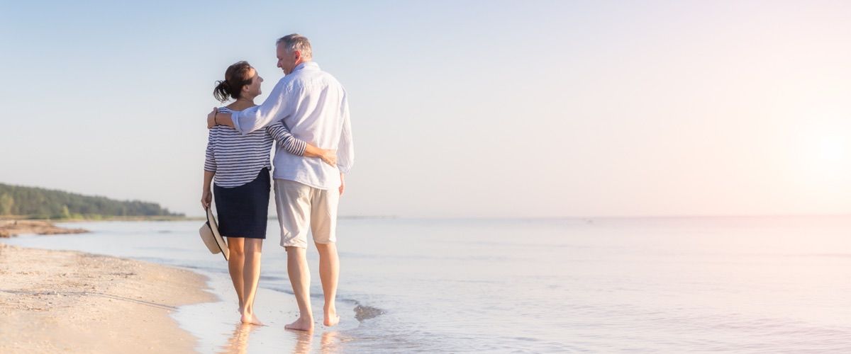 A retired senior couple taking a walk on the beach