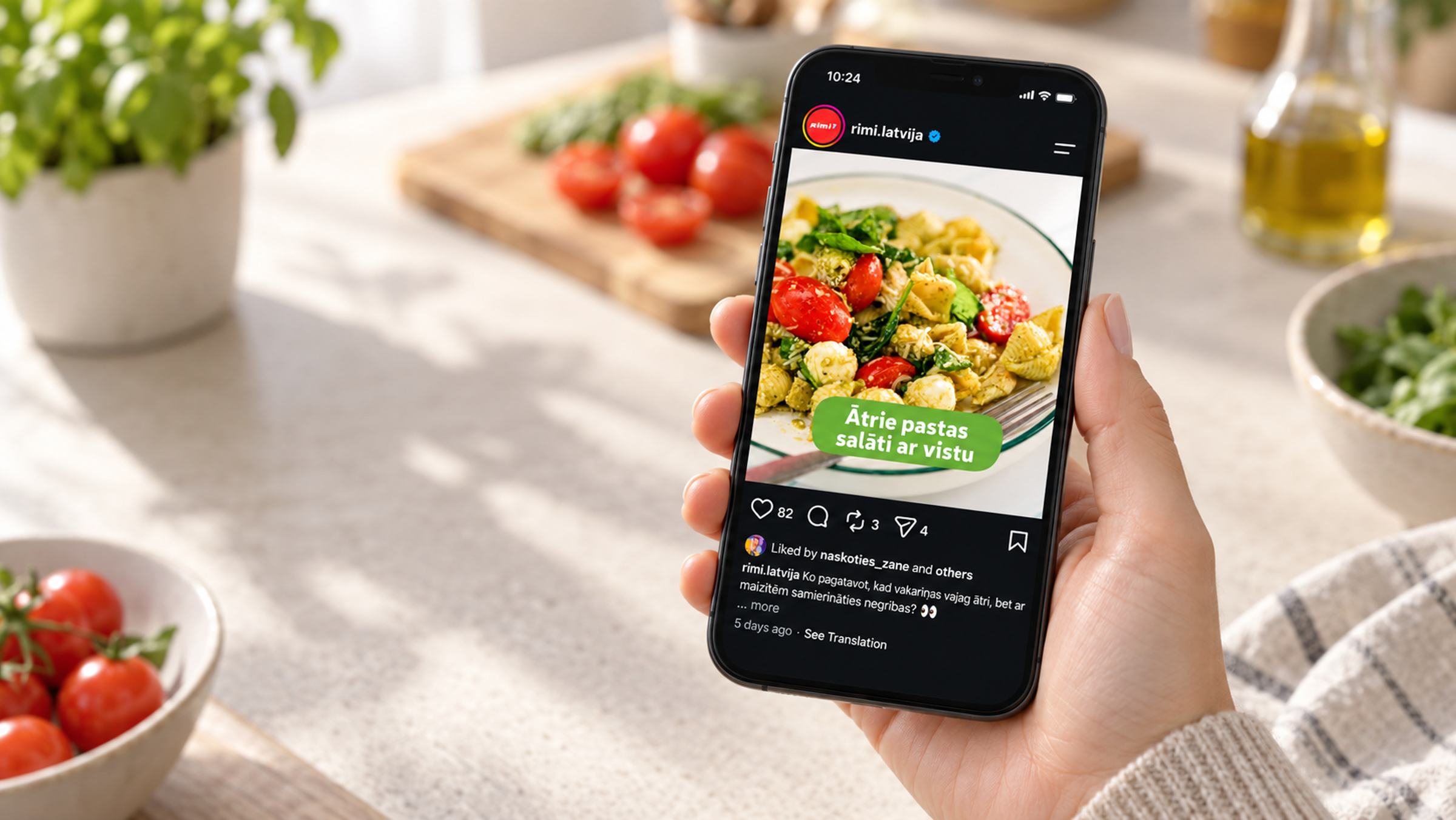 Cilvēks virtuvē tur viedtālruni ar Rimi Instagram ierakstu par vistas pastas salātiem.