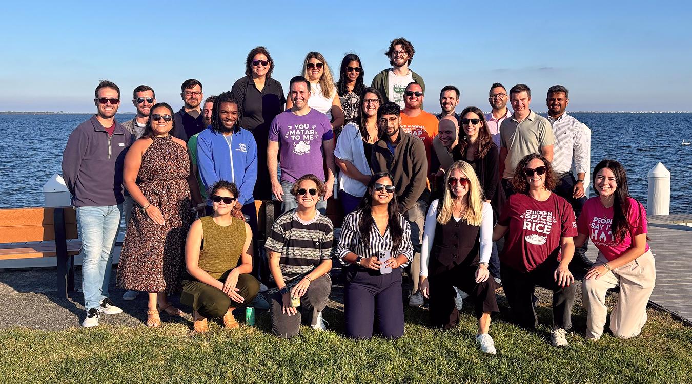 Team photo, large group of people smiling outdoors with ocean view behind them