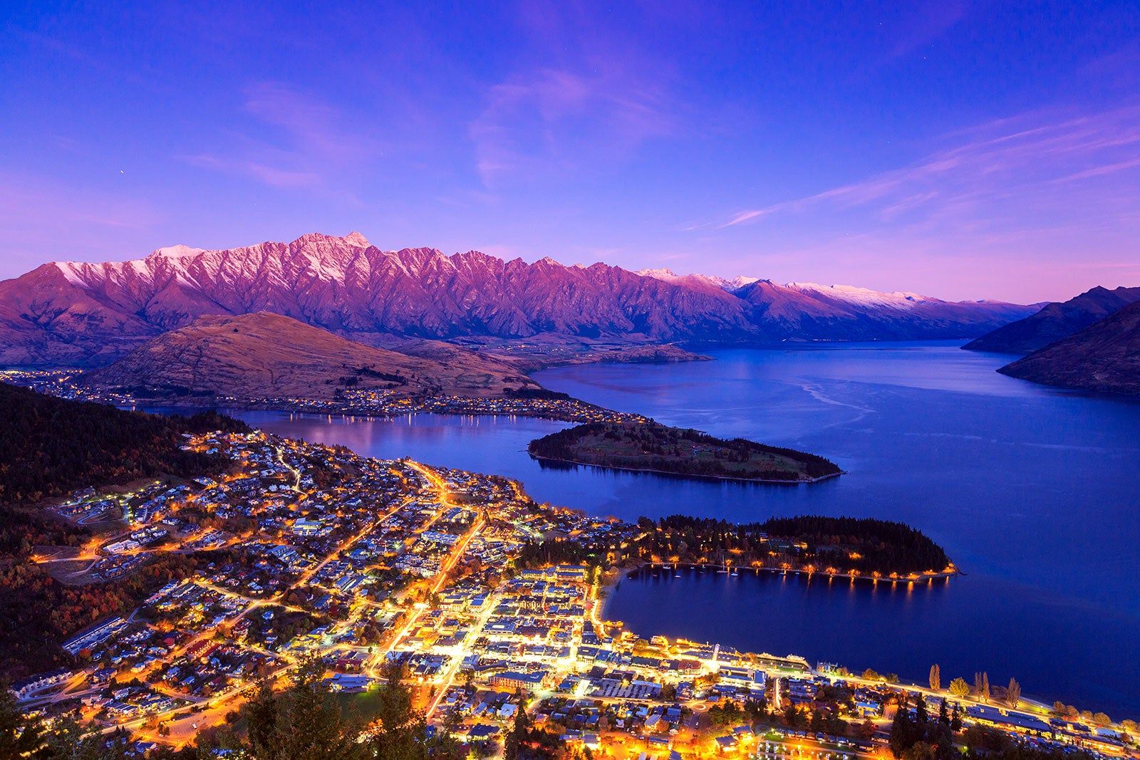 Ariel view of Queenstown at night with mountains and water.
