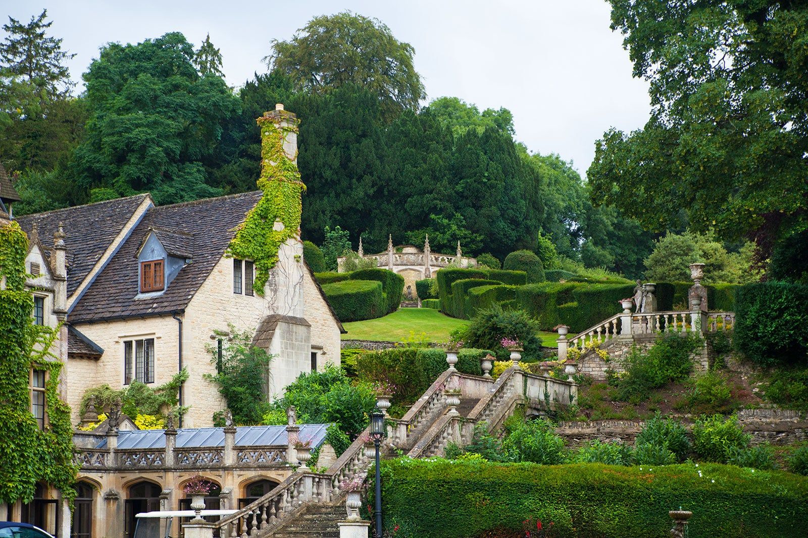 A manor house and an elaborate staircase and a bridge in hill-top garden.