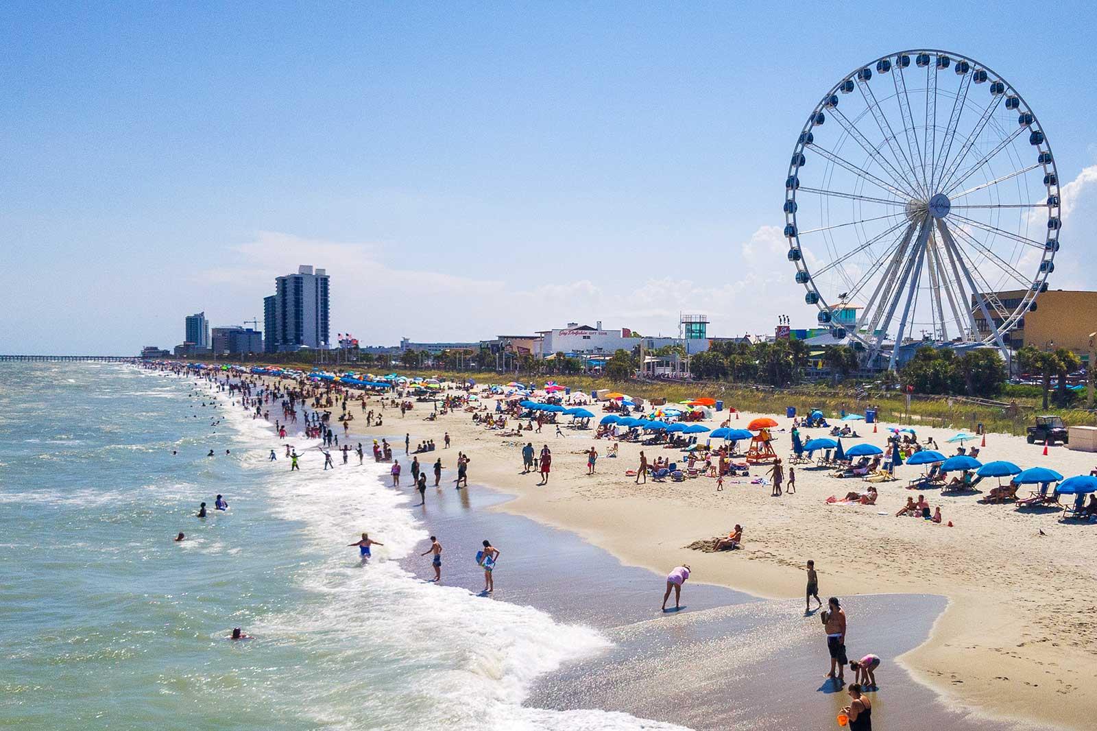 People along Myrtle Beach with the boardwalk and Ferris wheel.