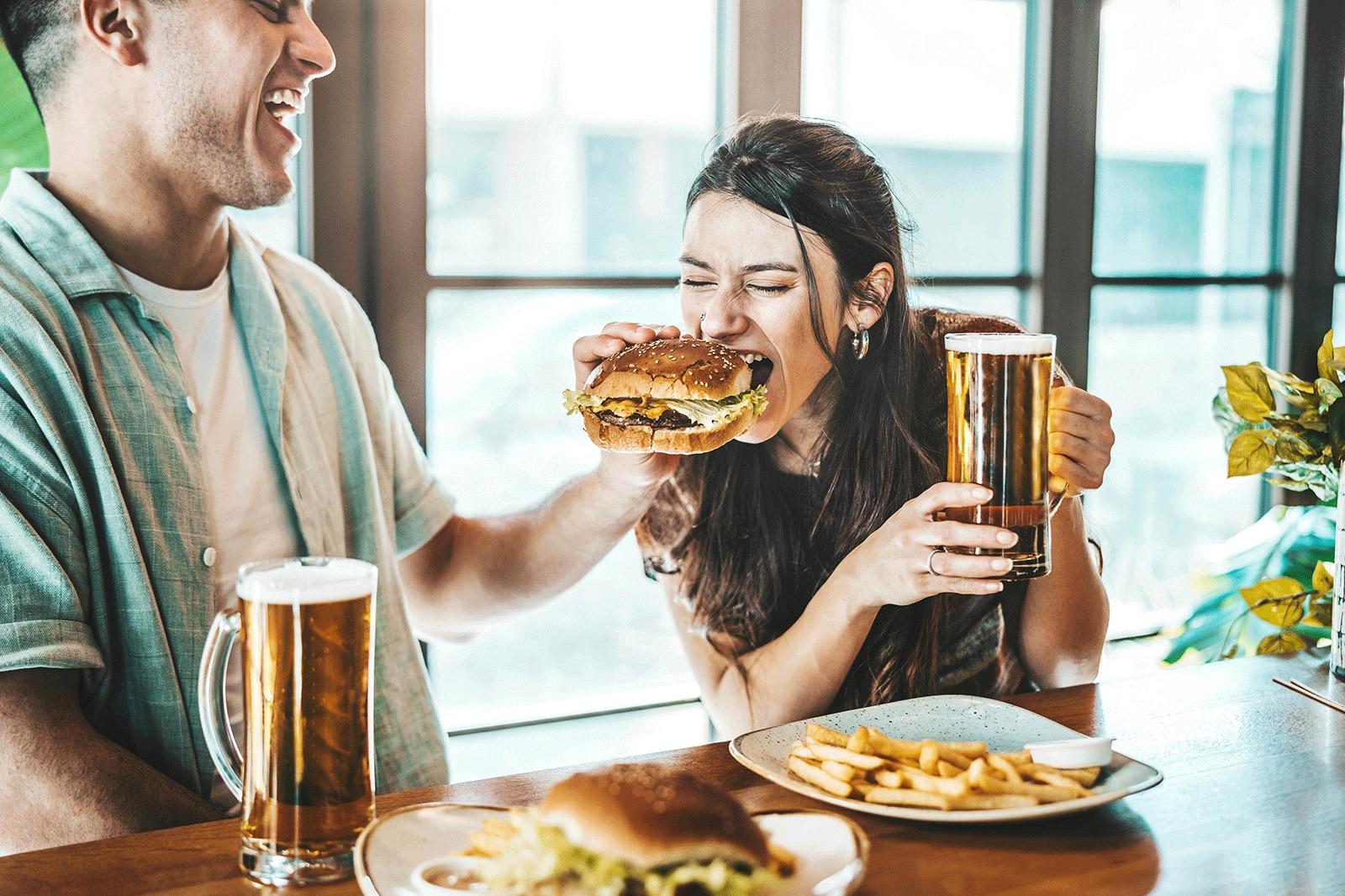 ↵A happy couple sharing a burger sitting in a restaurant.