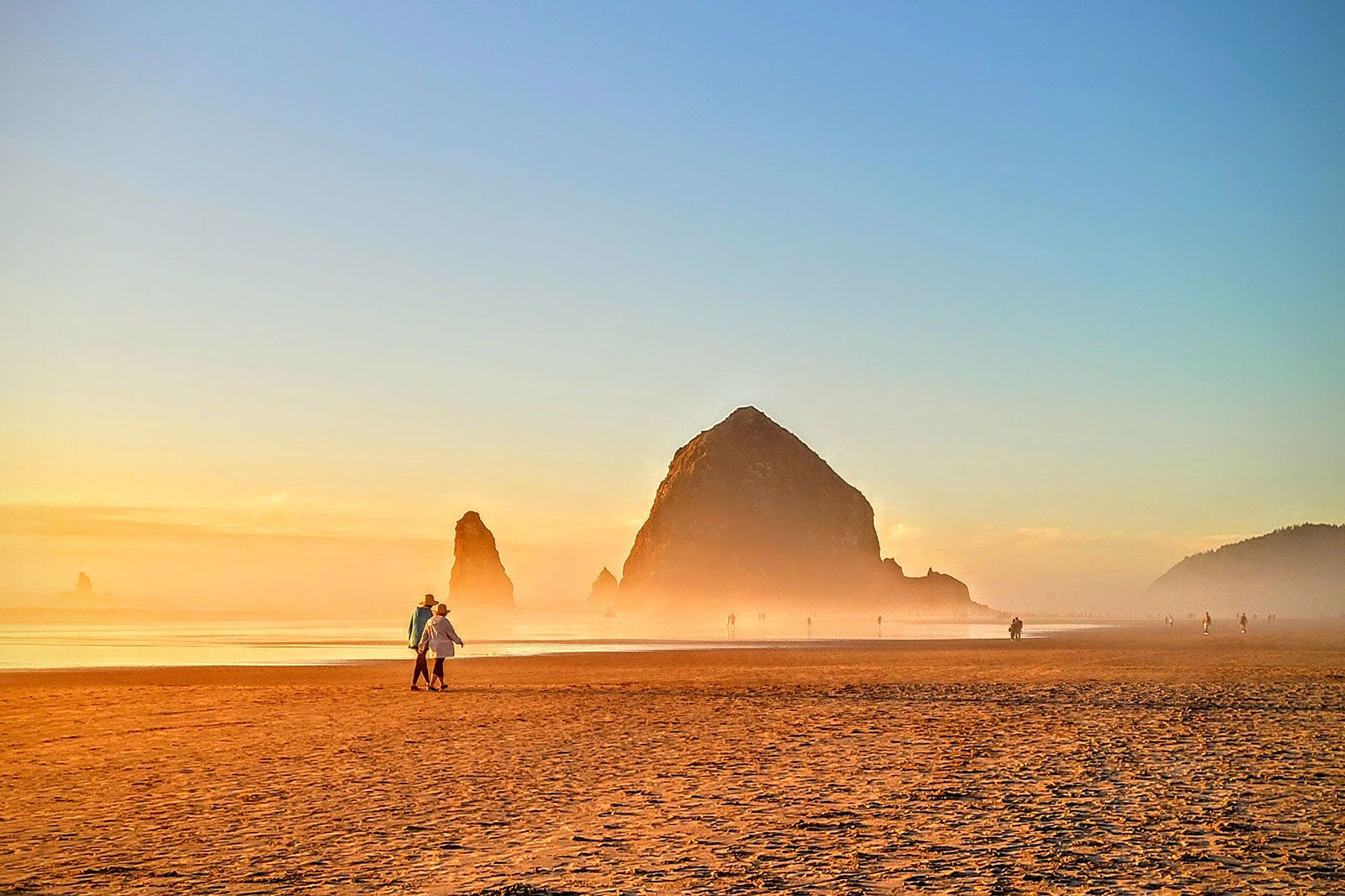 A hazy sunrise view of a large rock on a beach.