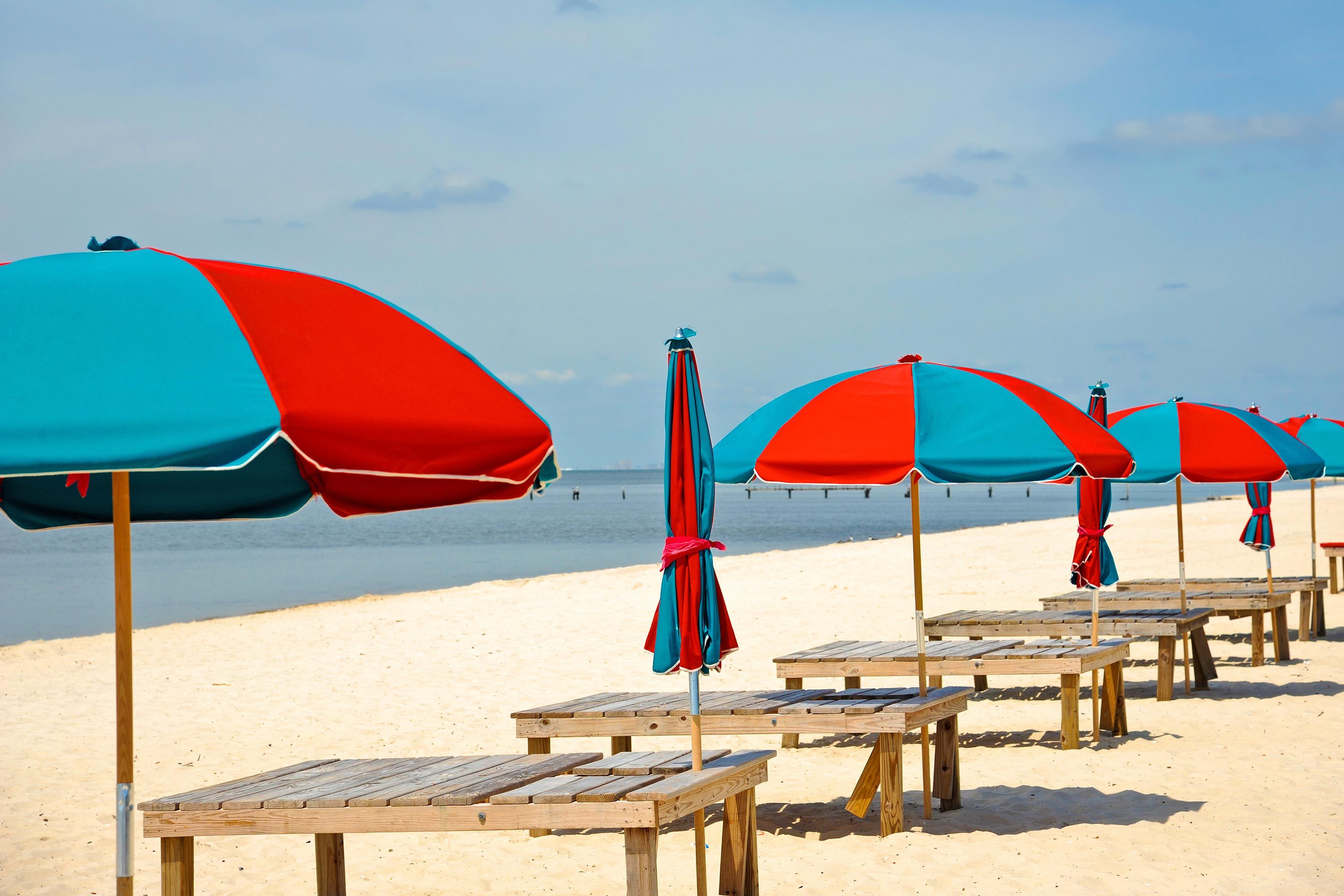 Red and blue umbrellas on the beach with wooden benches on Biloxi Beach in Mississippi.