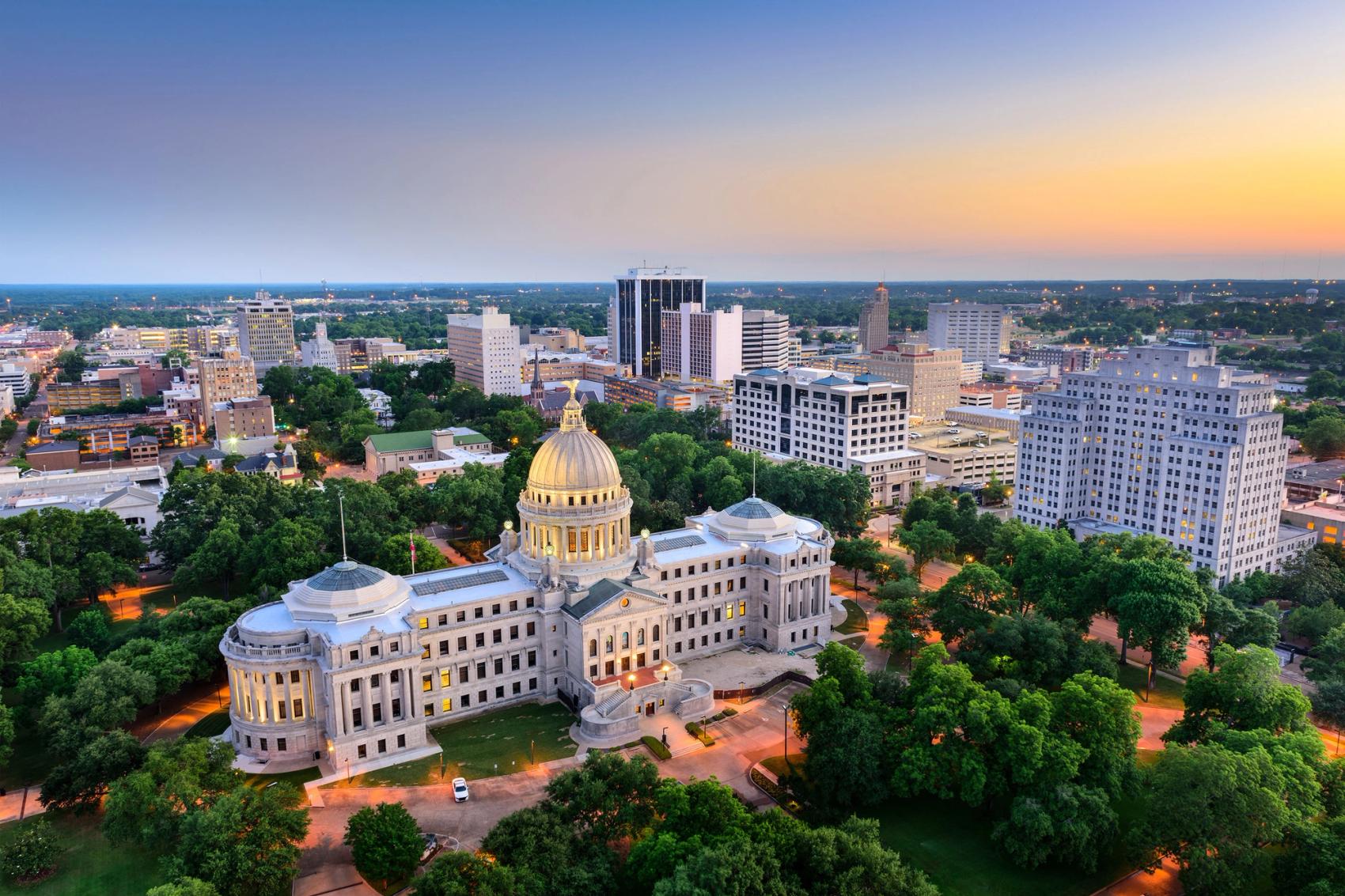 An aerial view of downtown area with a prominent neoclassical domed building with buildings and trees at sunset.