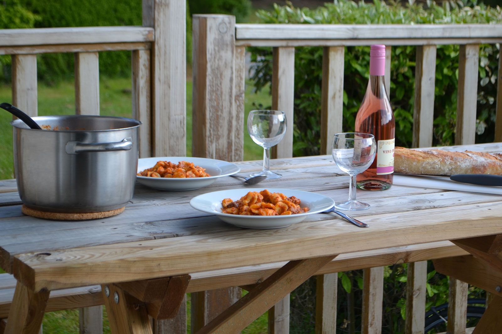 A bottle of Rose wine with two wine glasses, plates of food and bread kept on a table.