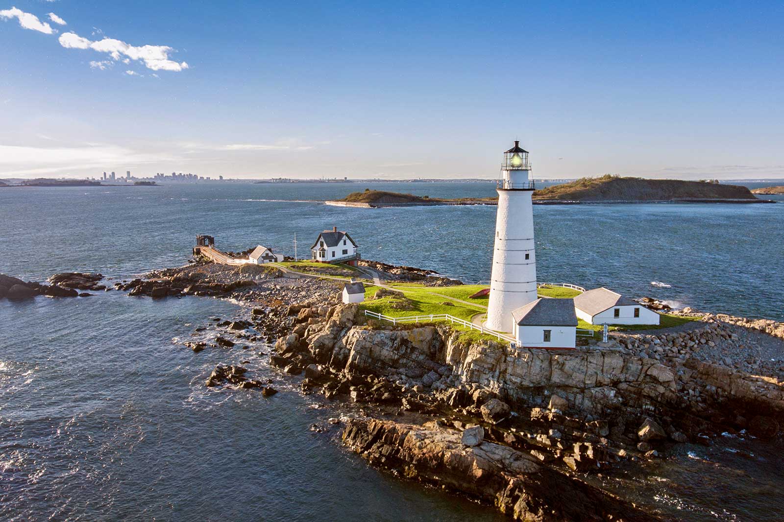 A white lighthouse, white houses, water, skyline of a city in the distance.