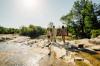 Three women walk on rocks crossing over a stream.