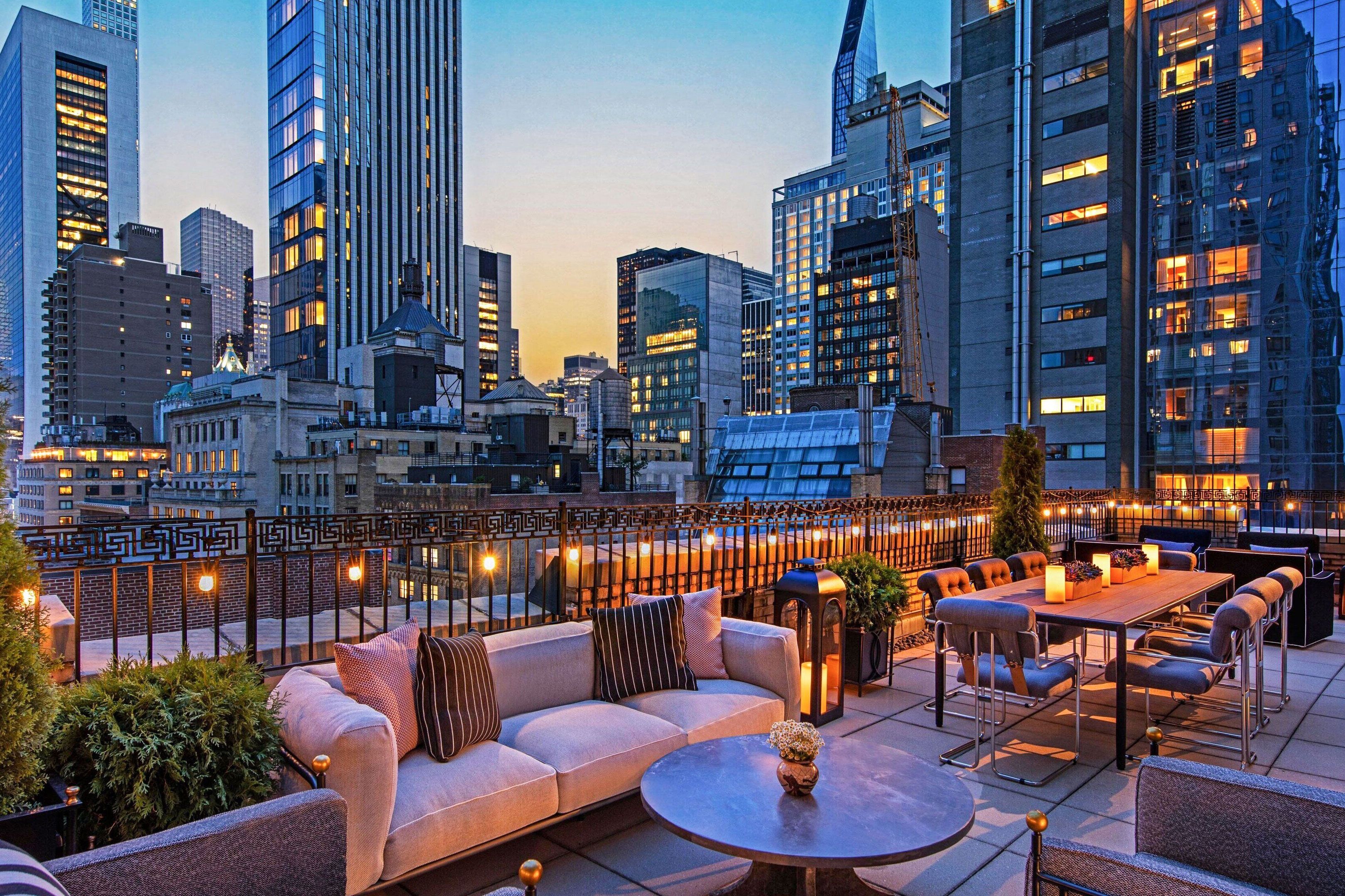 A rooftop terrace with lounge chairs, sofa and table, and views of New York City.