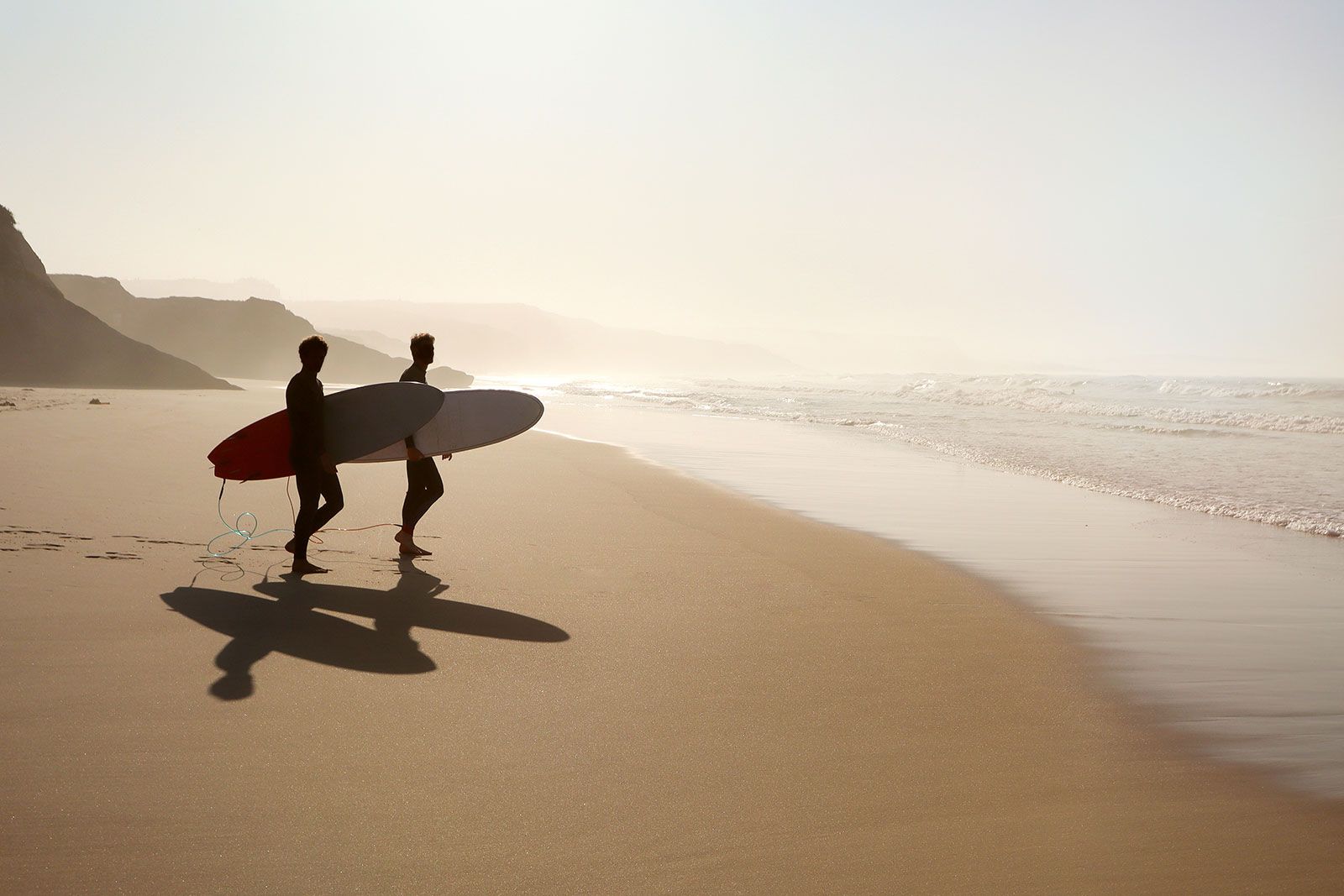 Two surfers with surfboards walk on the beach.