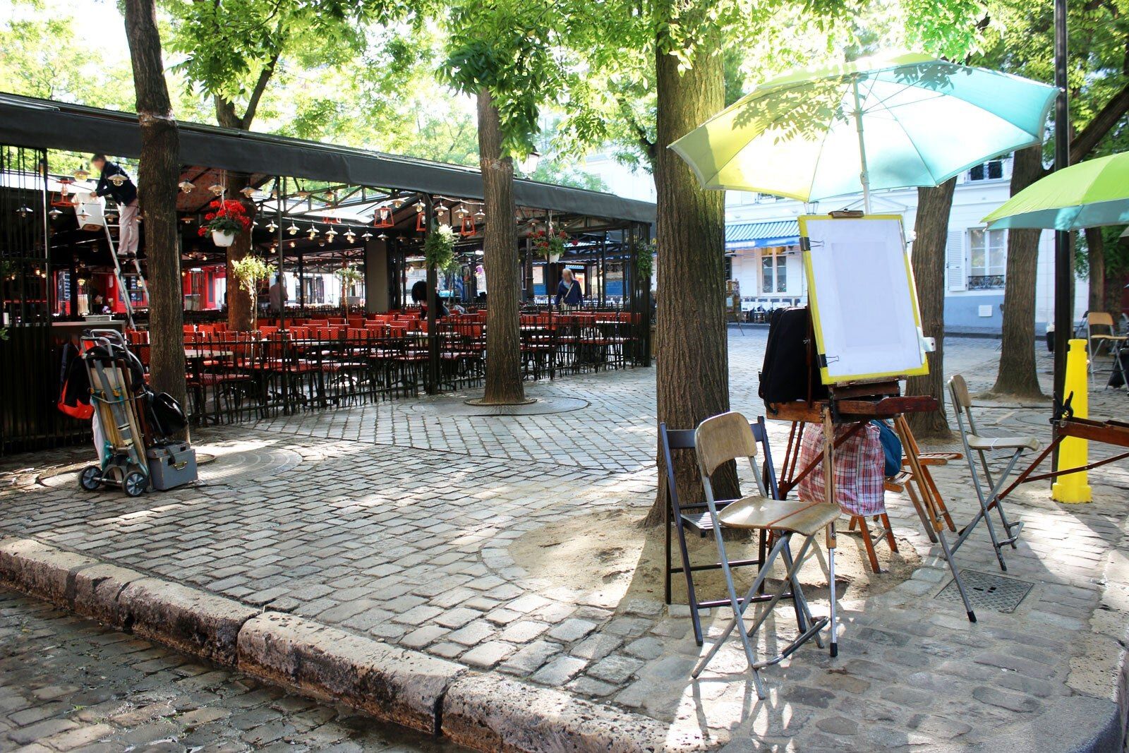 An artist's easel and café on a cobbled square.