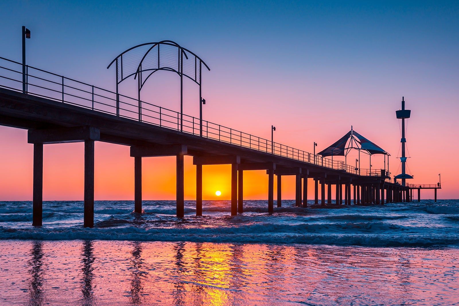 Vibrant pink and yellow sunset behind a pier. 