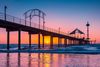 Vibrant pink and yellow sunset behind a pier.