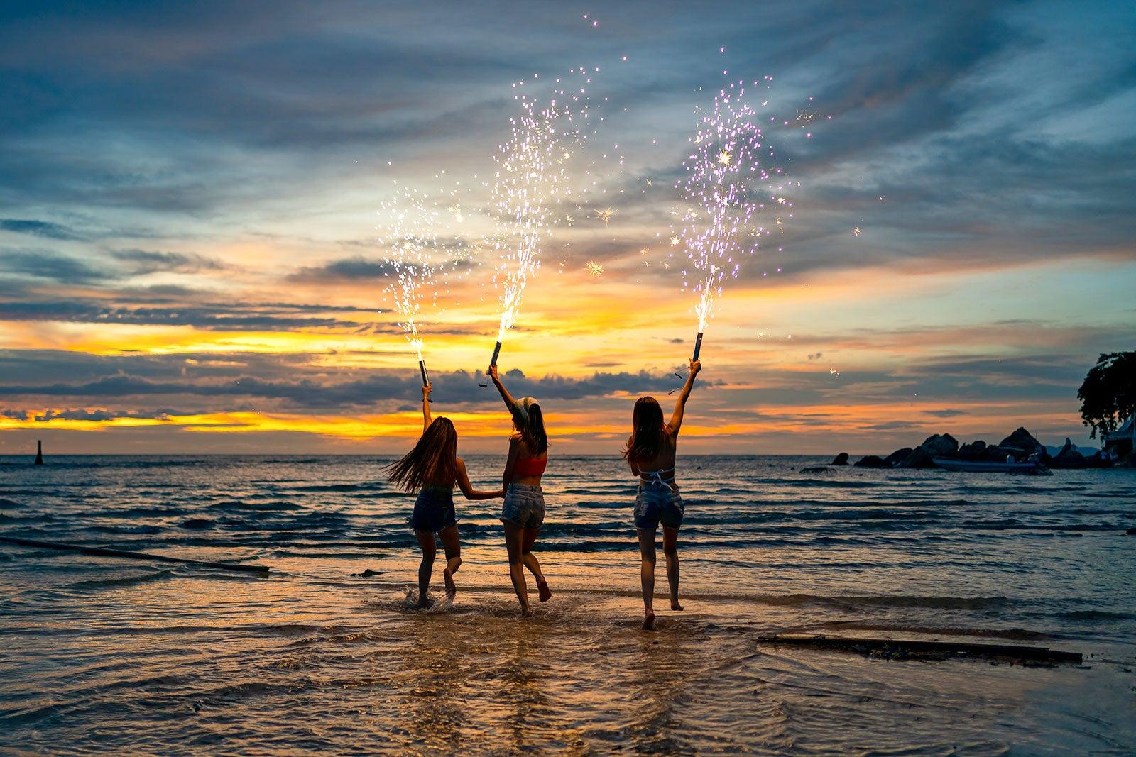 Women celebrating on a beach with sparklers.