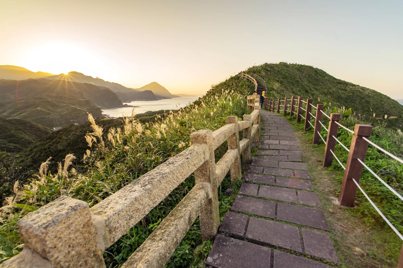 A brick walking trail with stone and wood railings leading over the mountains of Taipei.