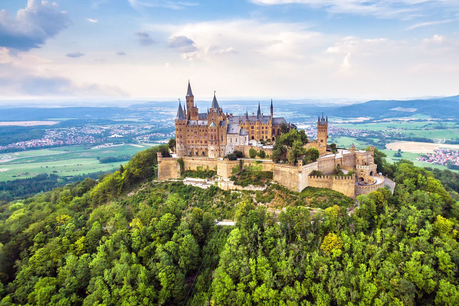 A castle on mountain top with green trees on the grounds.