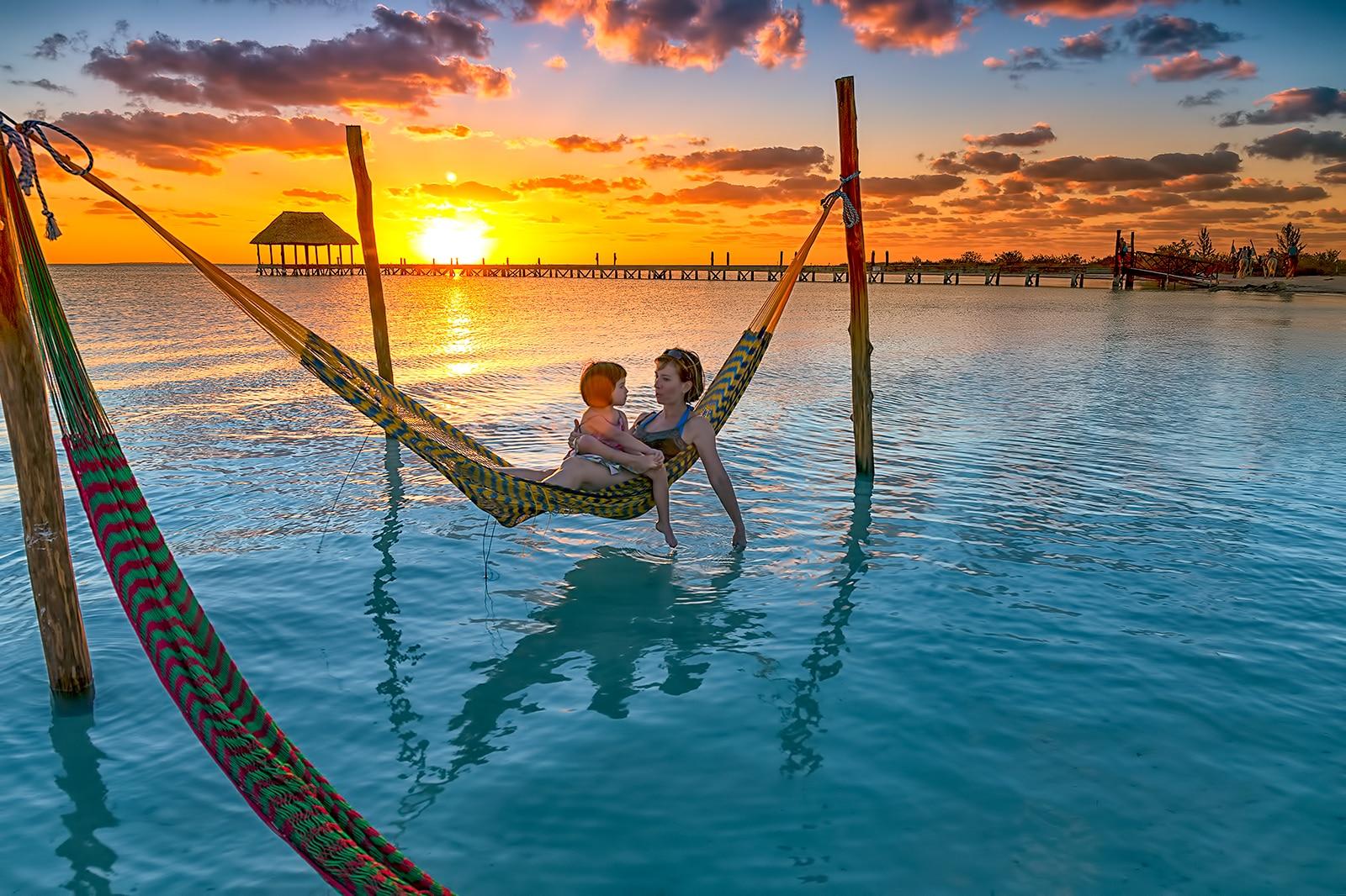 A parent and a child lounging in a hammock at sunset.