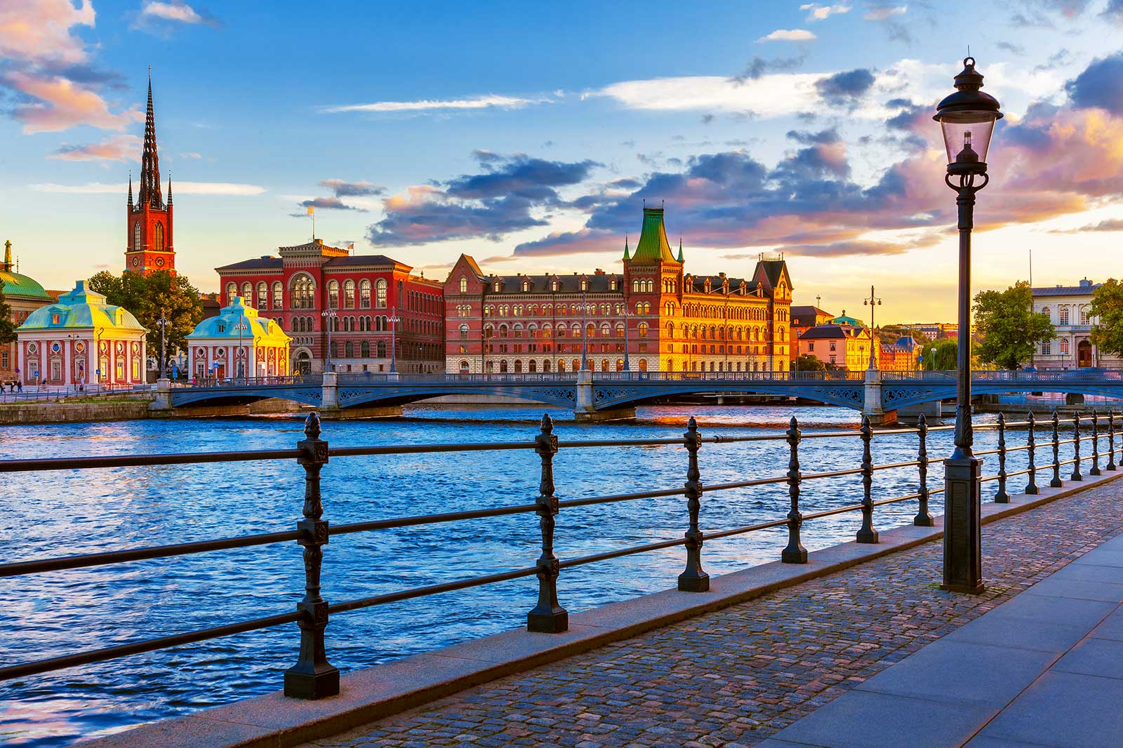 A cobbled waterside street in the foreground, Stockholm's old buildings and church tower in the background.