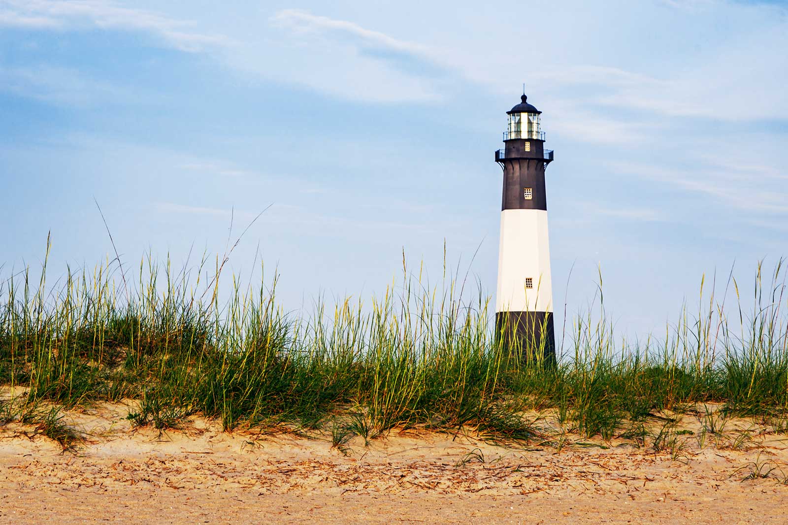 A black and white lighthouse at a beach.