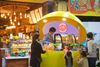A couple of kids with their mothers buying juice at an indoor food stall.