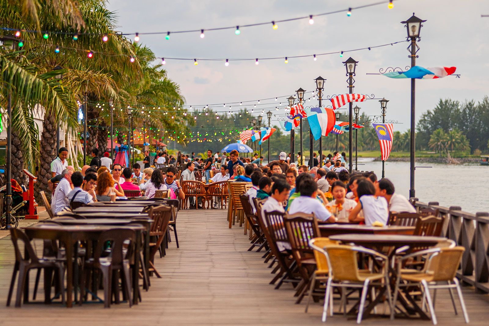 People eat food at tables by the water.