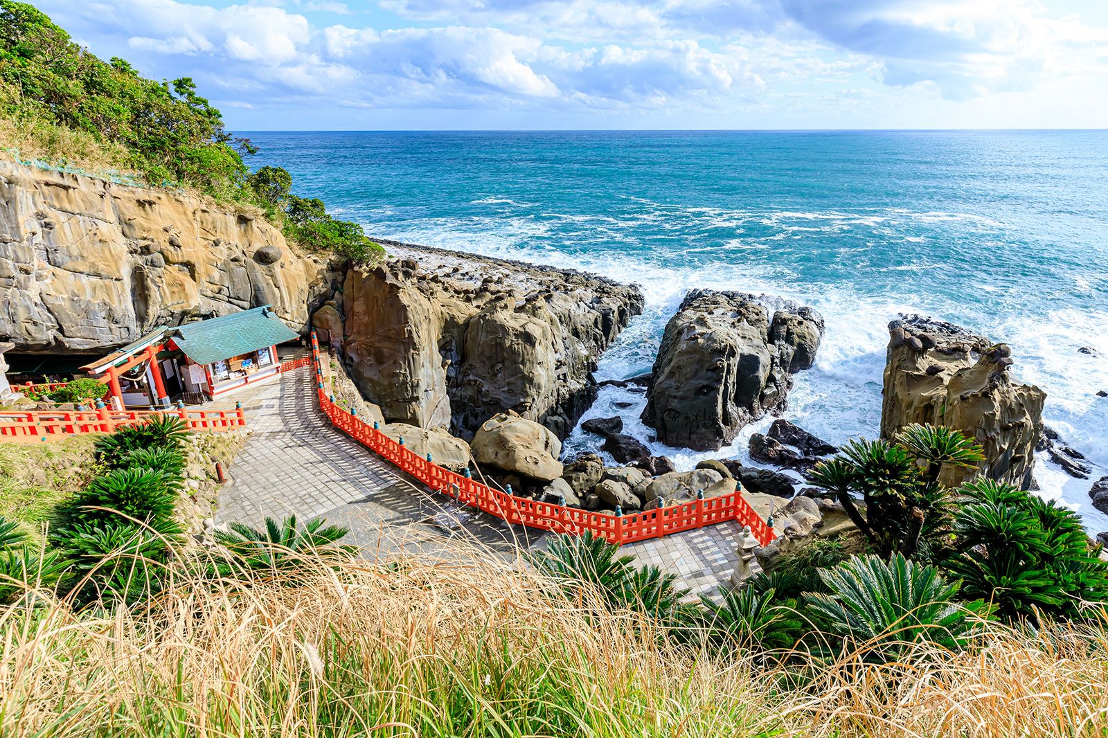 A temple with red fencing along a coastal cliff. 