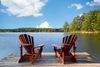 Two Adirondack chairs sitting on the end of a dock.