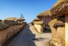 A village road passing between mud and thatched houses.