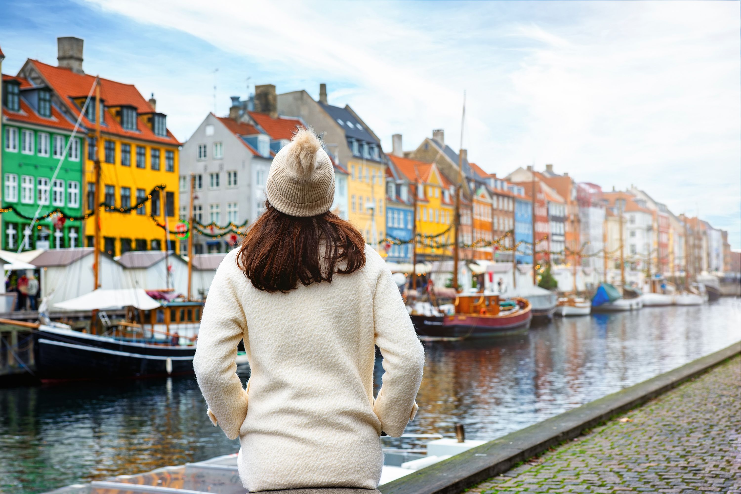 Rear view of a woman wearing a winter hat with the colorful buildings of Nyhavn, Denmark during Christmas.