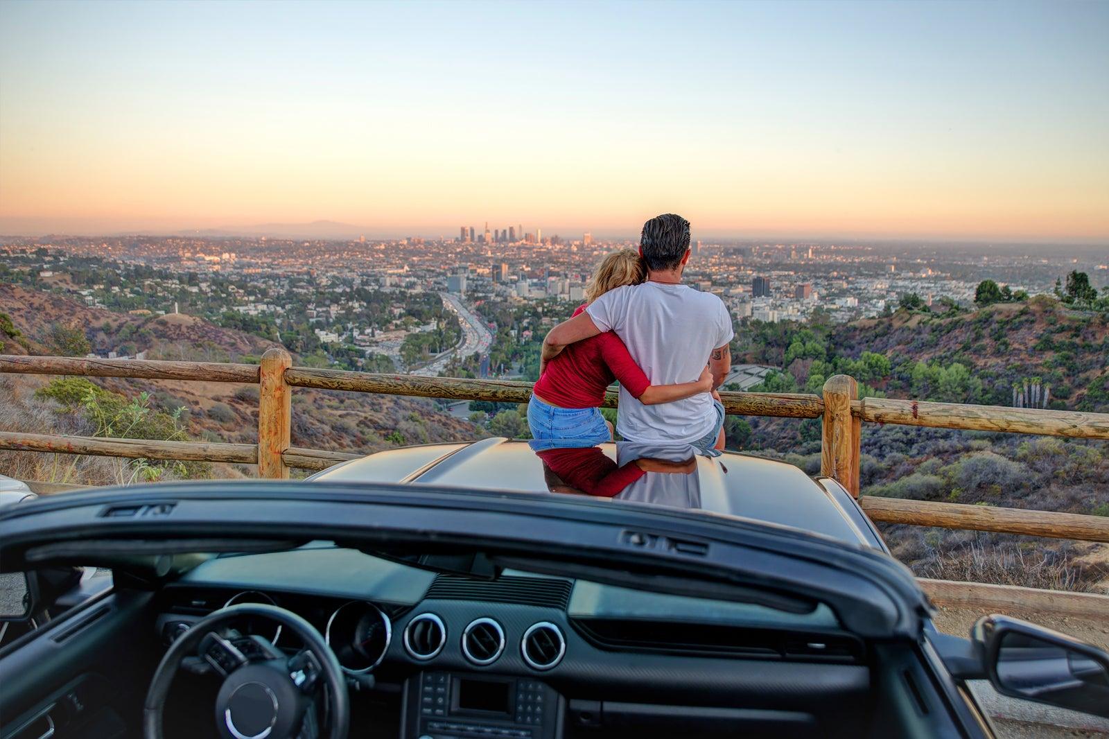 A couple on top of a car watching the sunset.