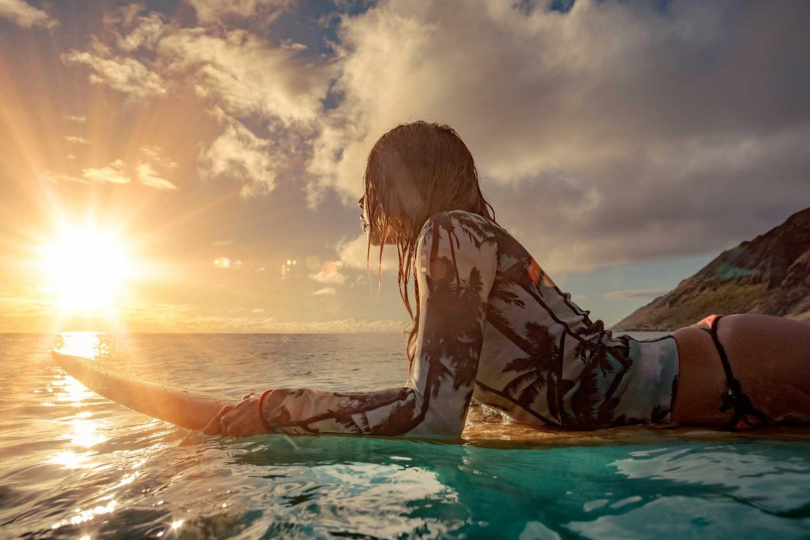 Woman on a surfboard waiting for a wave at sunrise.