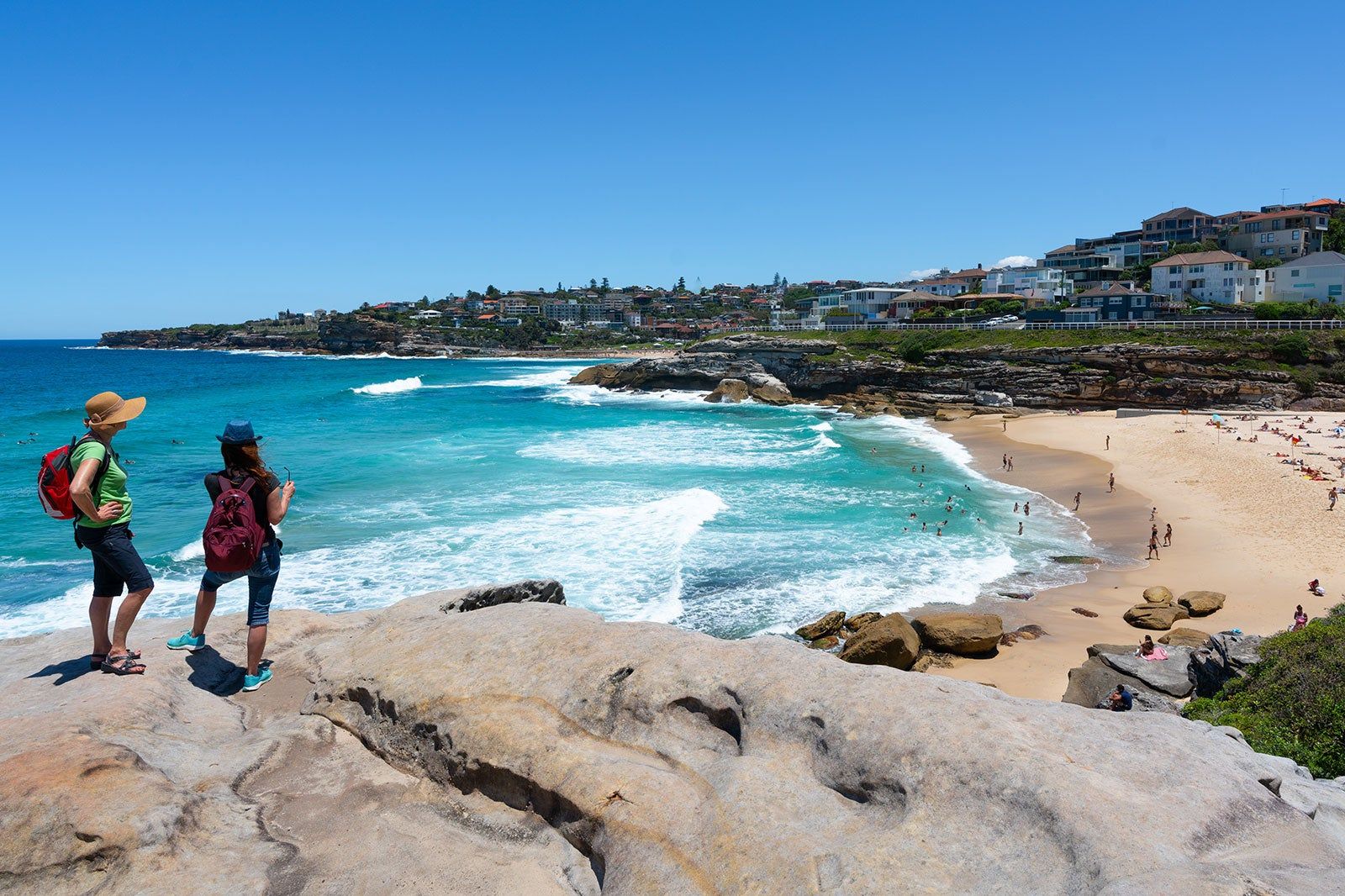 People on a hiking path above a beach and ocean view.