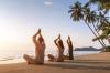 A small group of people sitting on the beach doing yoga with palm trees in the background.