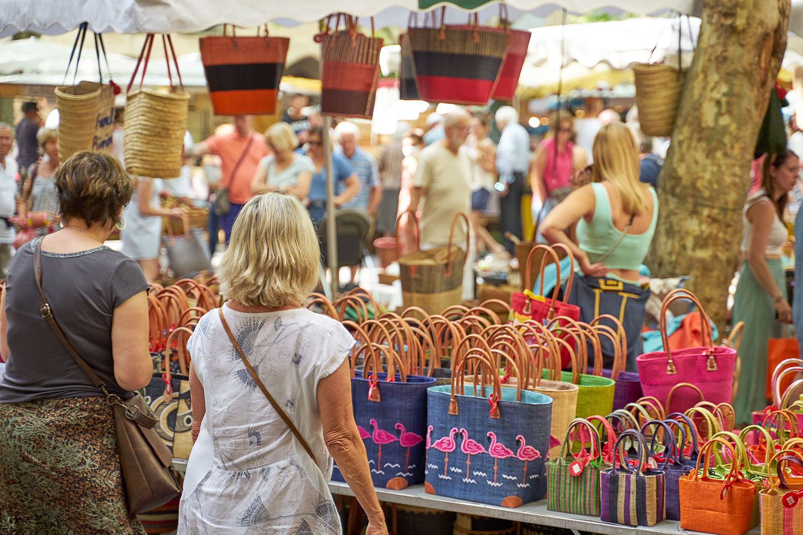 A crowd of people looking at the handbags at the market.