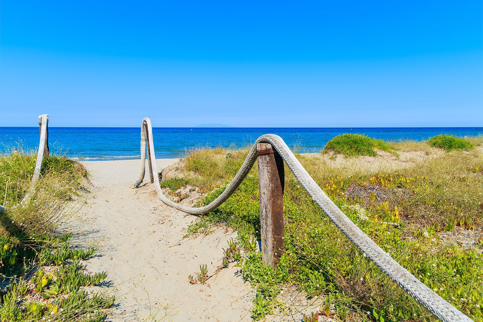 A path to sandy beach with blue water ocean and blue sky.