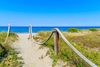 A path to sandy beach with blue water ocean and blue sky.