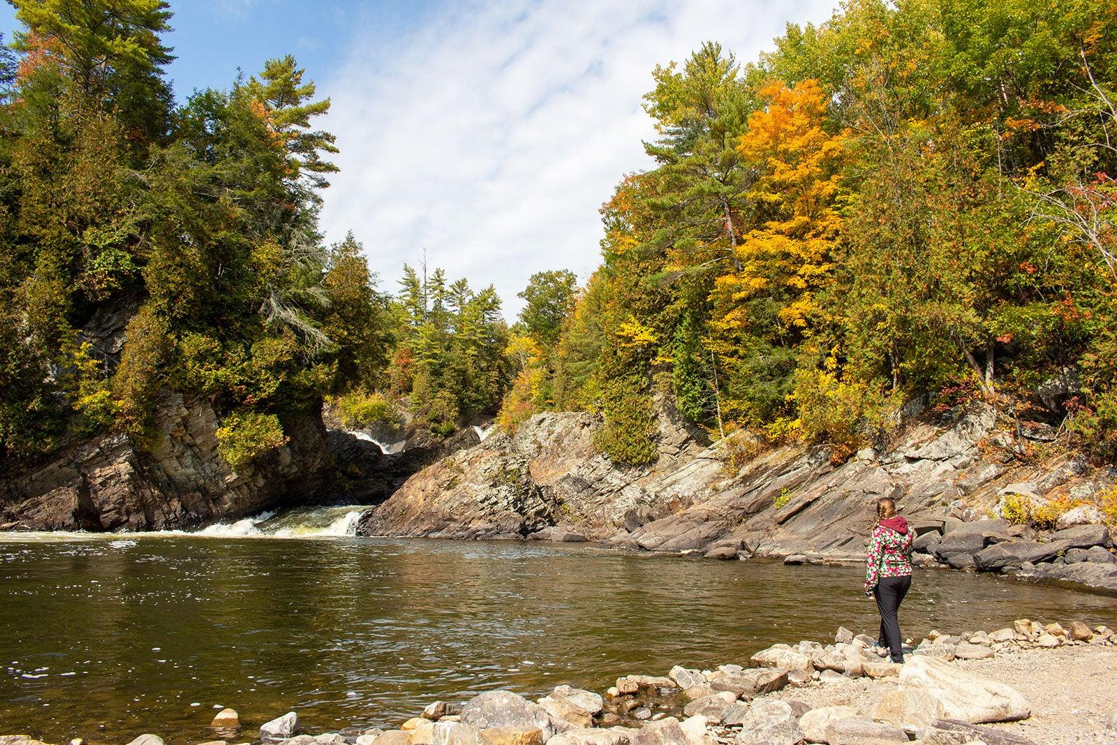 Person standing by a body of water with a small waterfall.