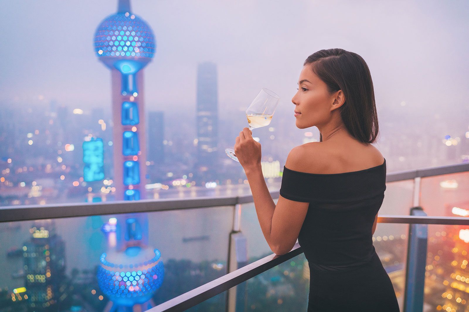 A person enjoying a cocktail at a rooftop bar at night.