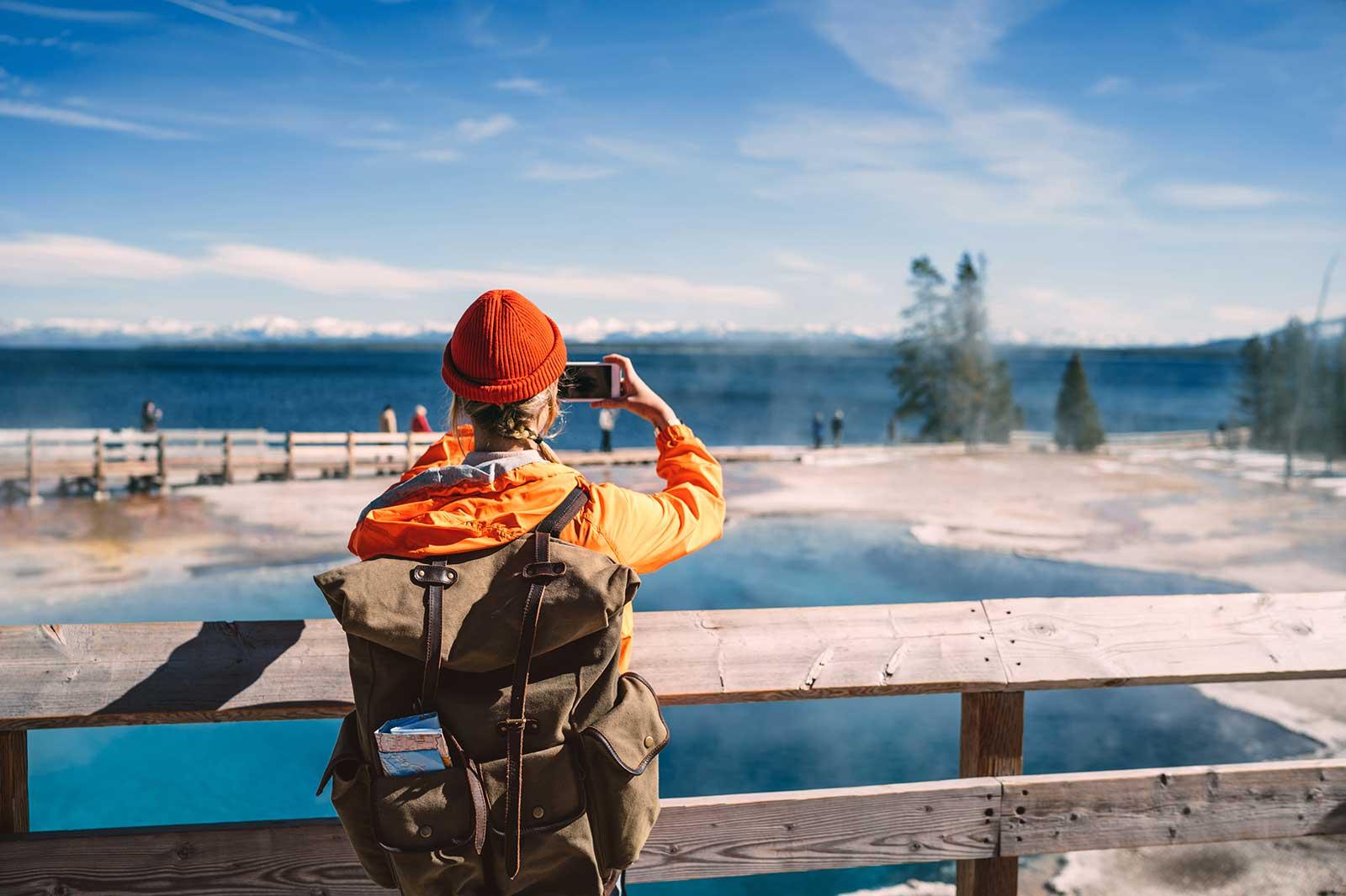Person with a backpack and a map taking a photo of a lake and mountains.